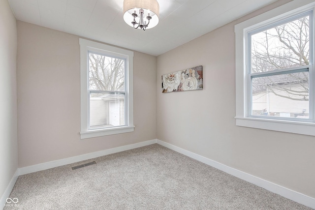 carpeted spare room with visible vents, baseboards, and an inviting chandelier