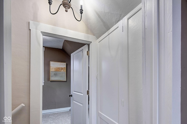 hall with carpet, baseboards, vaulted ceiling, and a textured ceiling