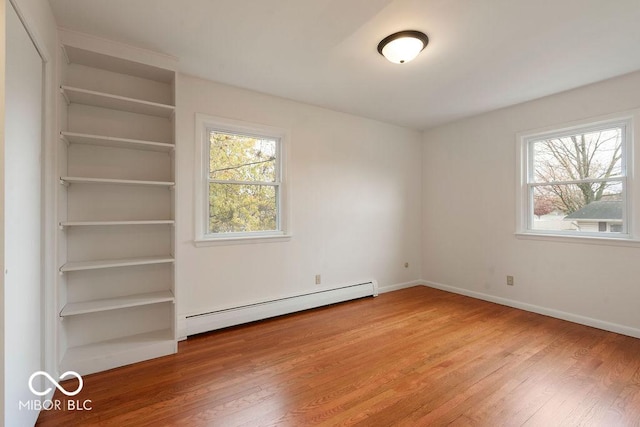 unfurnished bedroom with a baseboard heating unit, wood finished floors, and baseboards