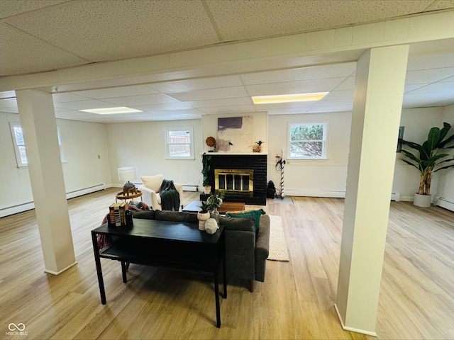 living room with a brick fireplace, a drop ceiling, light wood finished floors, and a healthy amount of sunlight