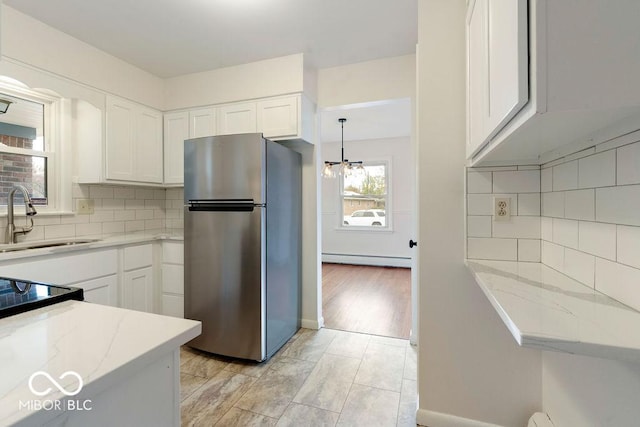 kitchen with white cabinets, light stone counters, freestanding refrigerator, baseboard heating, and a sink