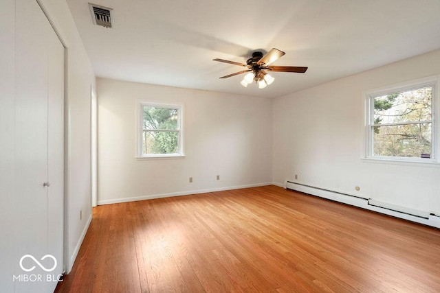 empty room with visible vents, a baseboard heating unit, a ceiling fan, light wood-type flooring, and baseboards