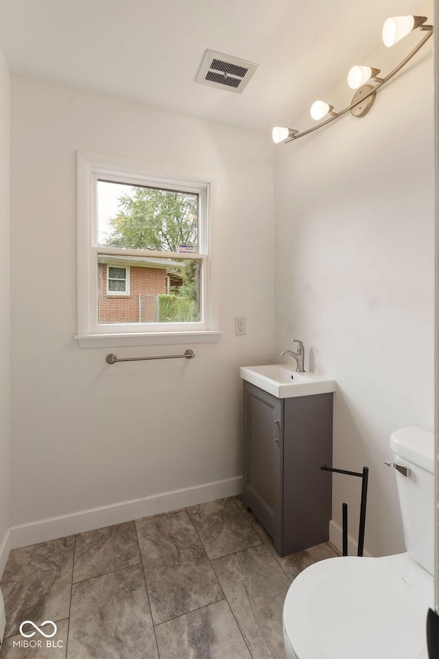 half bath featuring baseboards, visible vents, vanity, and toilet