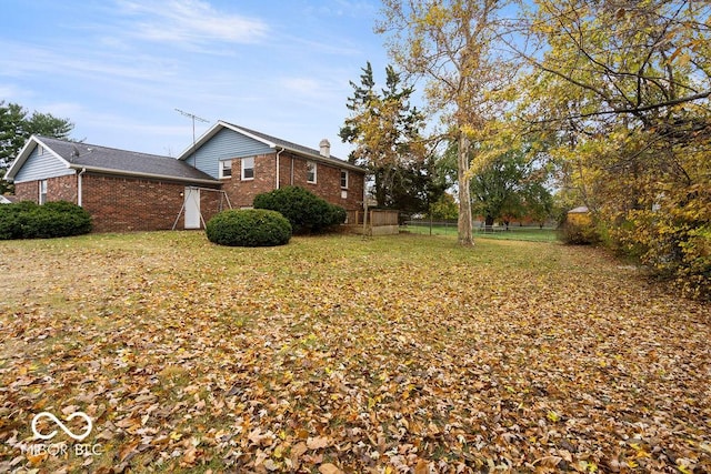 view of side of property featuring a chimney, fence, a lawn, and brick siding