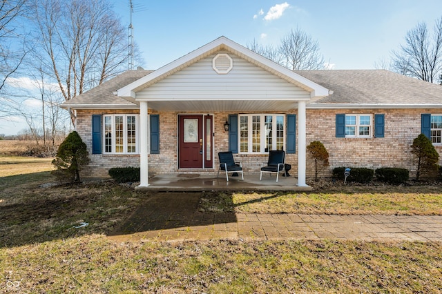 view of front facade with a shingled roof, a front yard, a porch, and brick siding