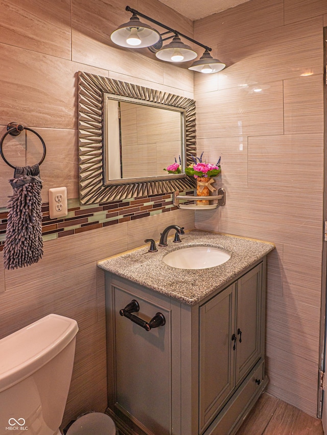 bathroom with toilet, wood finished floors, vanity, and tile walls