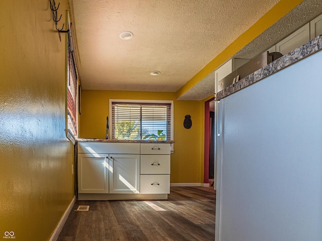 hall with visible vents, dark wood finished floors, a textured ceiling, and baseboards