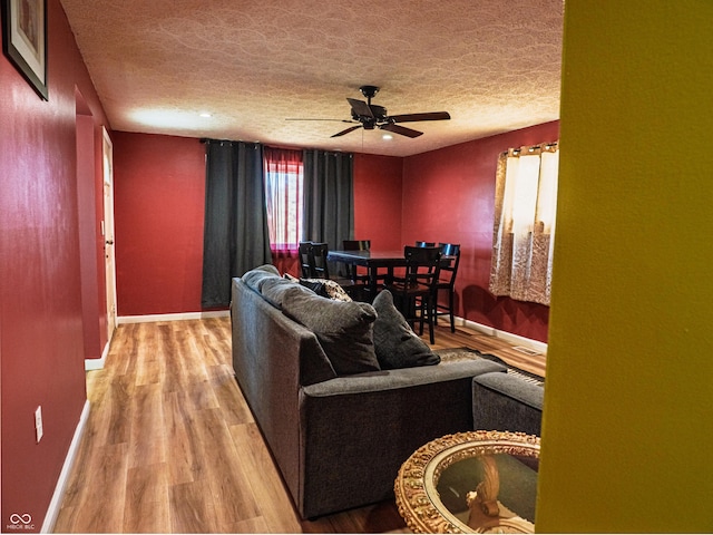 living area featuring a textured ceiling, baseboards, a ceiling fan, and light wood-style floors