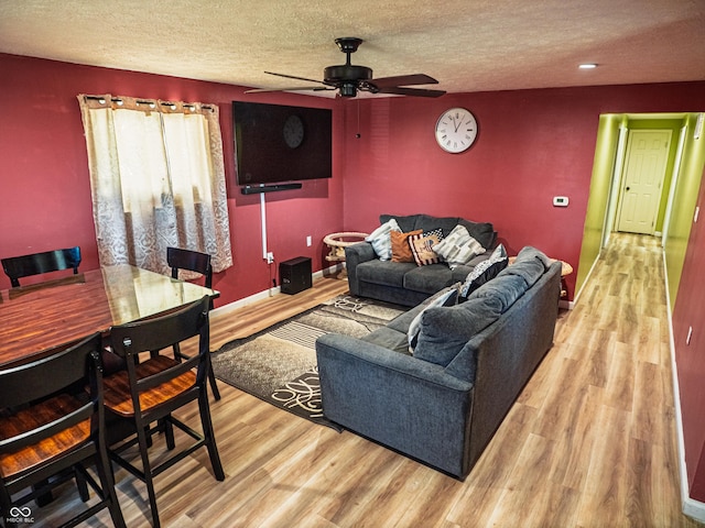 living room with a textured ceiling, a ceiling fan, light wood-style flooring, and baseboards