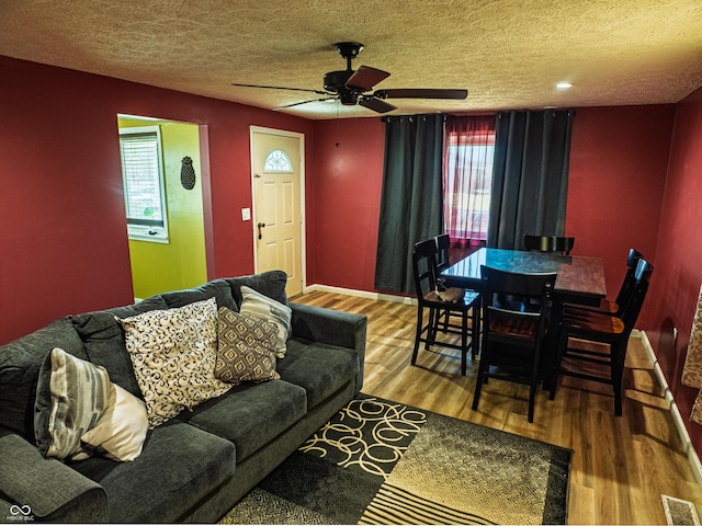 living room featuring a textured ceiling, wood finished floors, visible vents, baseboards, and a ceiling fan