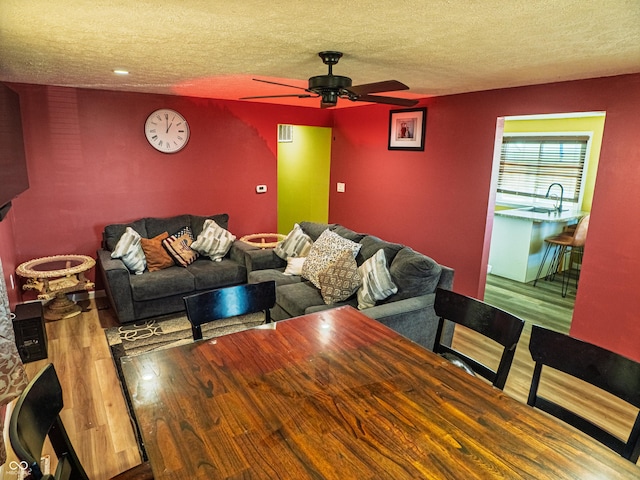 living room with ceiling fan, a textured ceiling, and wood finished floors