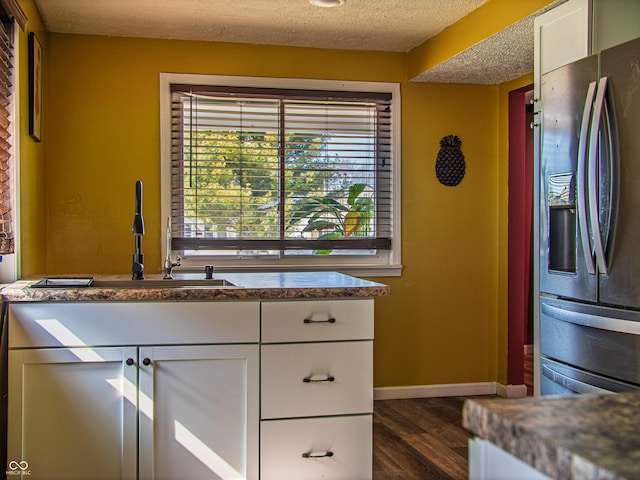 kitchen featuring dark wood-style flooring, stainless steel refrigerator with ice dispenser, white cabinetry, a textured ceiling, and baseboards