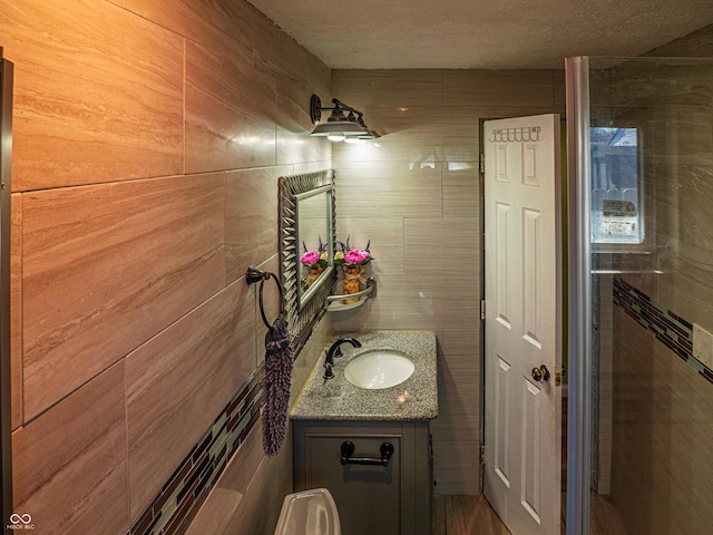 bathroom featuring a textured ceiling, vanity, and tile walls