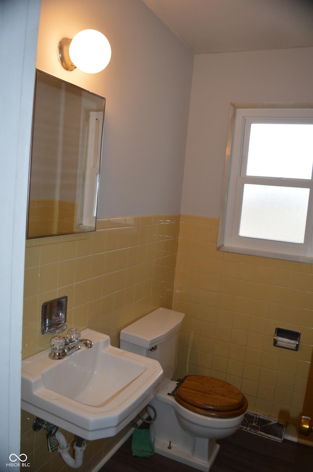 bathroom featuring toilet, a wainscoted wall, tile walls, and a sink