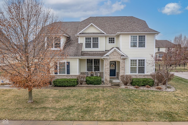 view of front of home featuring stone siding, covered porch, roof with shingles, and a front lawn