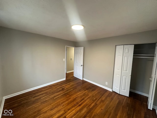 unfurnished bedroom featuring dark wood-style flooring, a closet, and baseboards