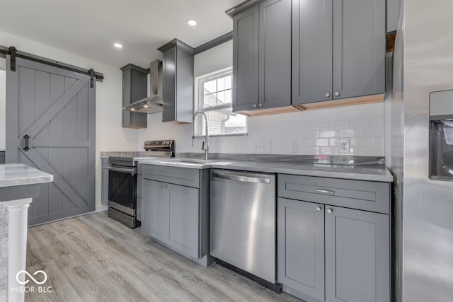 kitchen with a barn door, gray cabinets, stainless steel appliances, and a sink