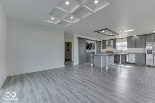 kitchen with a barn door, gray cabinetry, open floor plan, appliances with stainless steel finishes, and wall chimney range hood