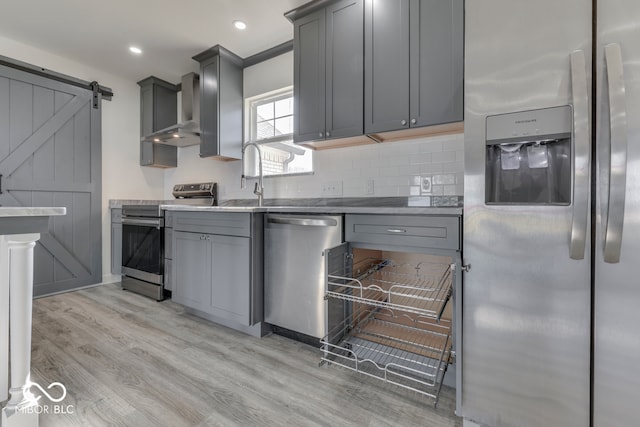 kitchen featuring stainless steel appliances, gray cabinets, wall chimney range hood, and a barn door