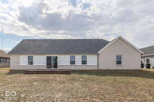 back of property with a shingled roof, brick siding, a lawn, and a deck