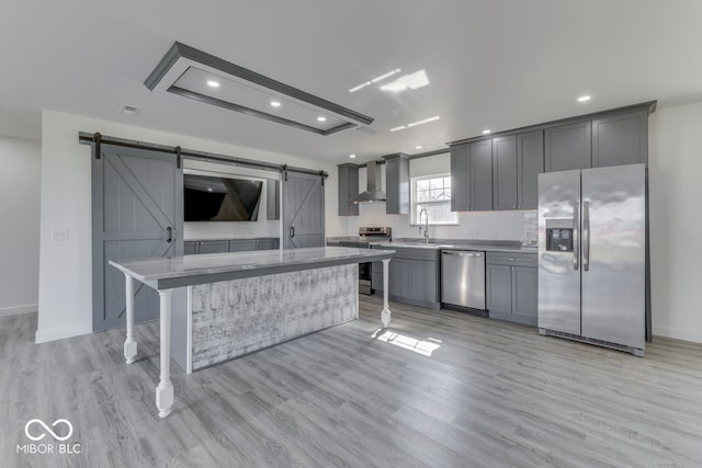 kitchen with light wood finished floors, a barn door, appliances with stainless steel finishes, a sink, and wall chimney exhaust hood