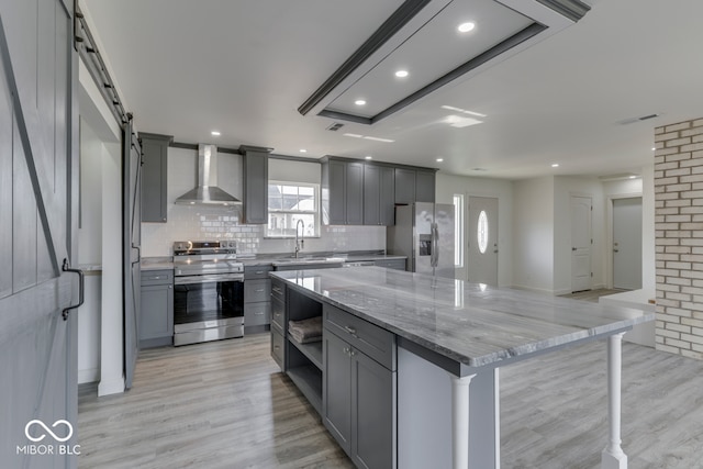 kitchen featuring a kitchen island, appliances with stainless steel finishes, gray cabinetry, wall chimney range hood, and a sink