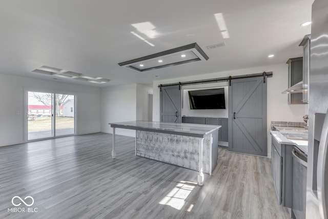 kitchen with a barn door, light wood-style flooring, light stone counters, open floor plan, and gray cabinets