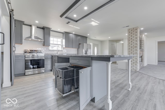 kitchen with gray cabinets, decorative backsplash, appliances with stainless steel finishes, a kitchen island, and wall chimney exhaust hood