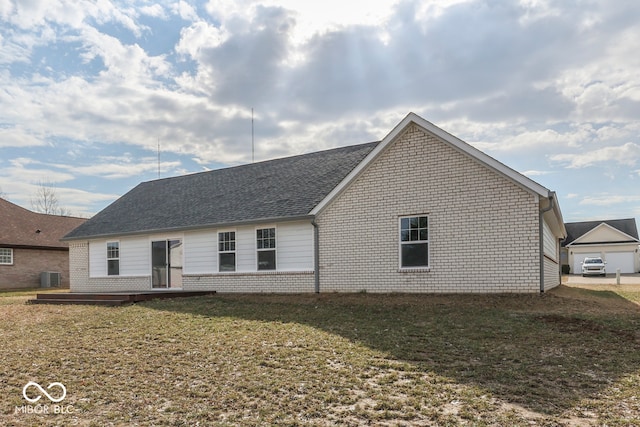 back of property featuring brick siding, a shingled roof, a lawn, central AC, and a wooden deck