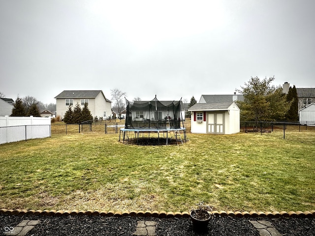 view of yard featuring an outbuilding, a fenced backyard, a residential view, a storage unit, and a trampoline