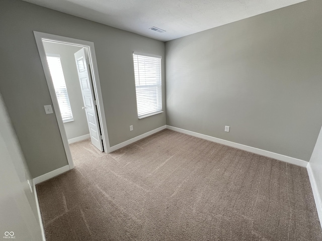 empty room with visible vents, light carpet, and baseboards