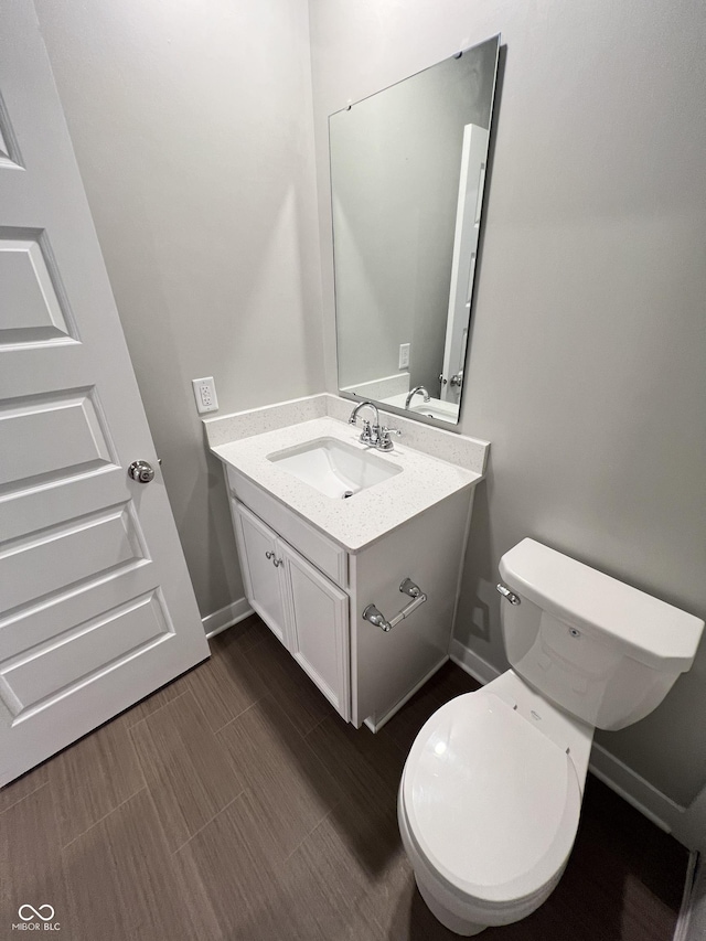 half bathroom with baseboards, vanity, and toilet