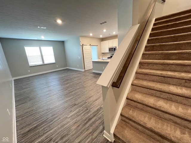 stairs with a barn door, visible vents, baseboards, wood finished floors, and recessed lighting