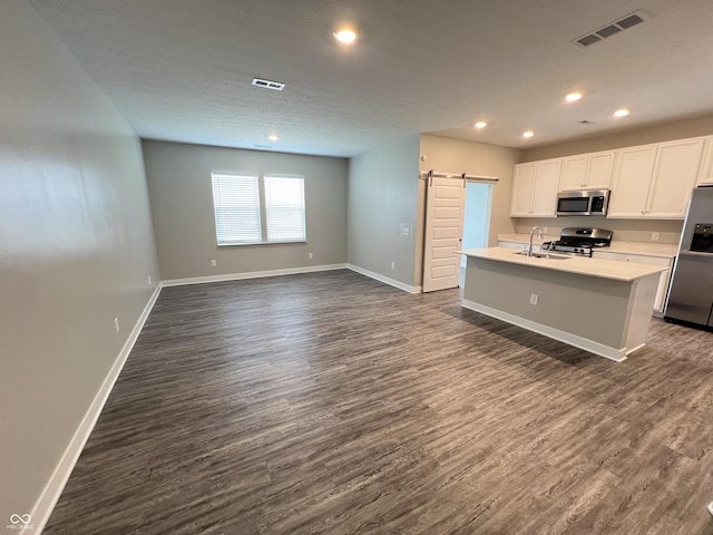 kitchen featuring a barn door, visible vents, an island with sink, stainless steel appliances, and light countertops