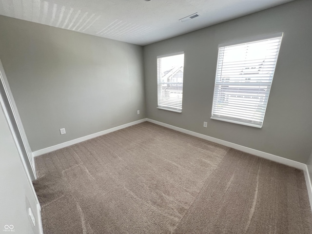 unfurnished room with carpet floors, visible vents, and baseboards