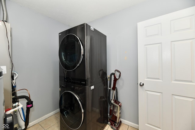 laundry area featuring stacked washer / dryer, laundry area, light tile patterned flooring, and baseboards