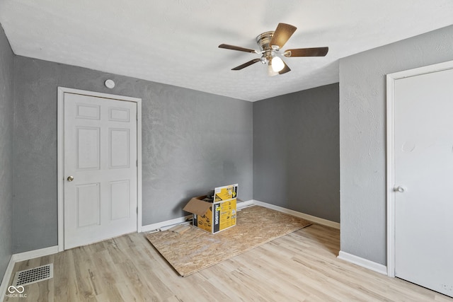 interior space with a textured wall, a ceiling fan, visible vents, baseboards, and light wood finished floors