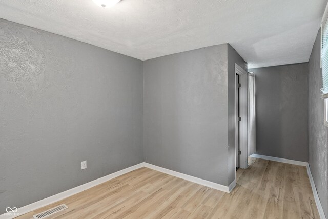 unfurnished room with a textured ceiling, a textured wall, visible vents, baseboards, and light wood finished floors