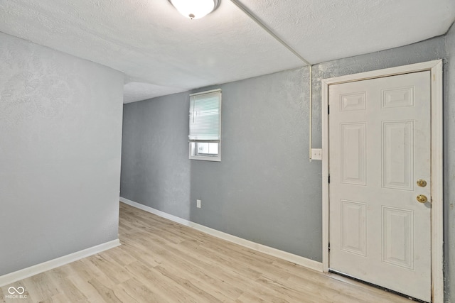 spare room with a textured ceiling, light wood finished floors, and baseboards