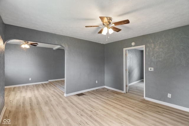 spare room with arched walkways, ceiling fan, light wood finished floors, and baseboards