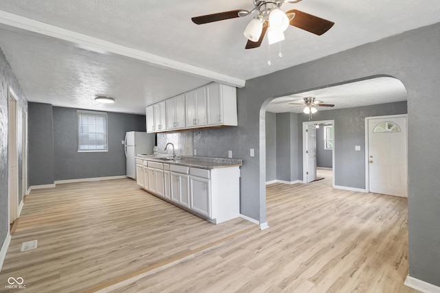 kitchen featuring light wood-style flooring, arched walkways, white cabinets, and a sink