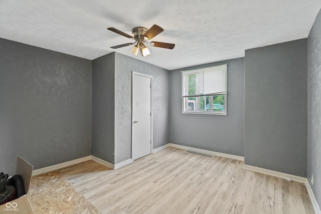 unfurnished bedroom featuring light wood-style floors, visible vents, a textured wall, and baseboards