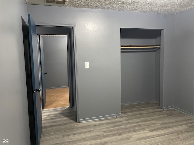 unfurnished bedroom featuring baseboards, wood finished floors, a closet, and a textured ceiling