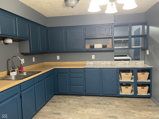 kitchen featuring a sink, light countertops, a textured ceiling, blue cabinets, and open shelves