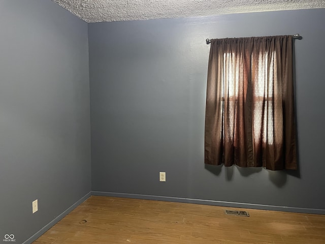 spare room featuring a textured ceiling, wood finished floors, visible vents, and baseboards