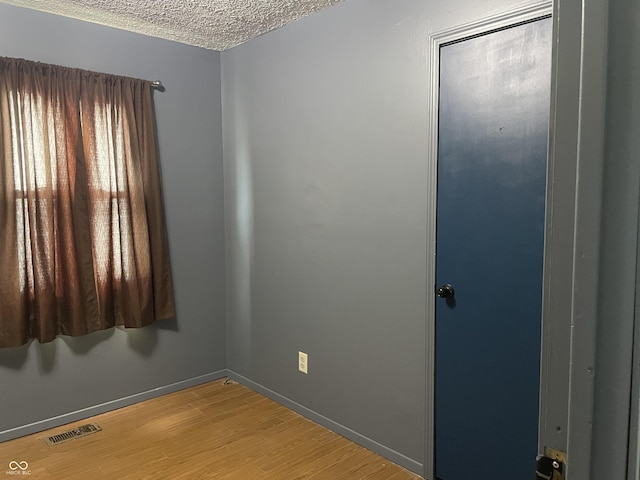 empty room with light wood-type flooring, visible vents, baseboards, and a textured ceiling