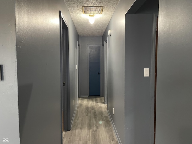 hall featuring visible vents, baseboards, a textured ceiling, and light wood finished floors