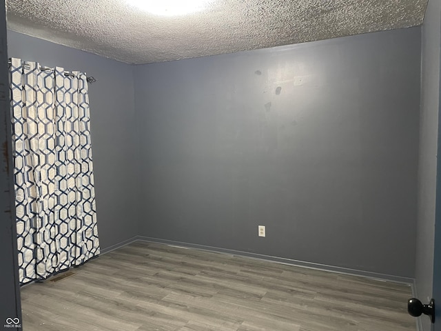 unfurnished room with wood finished floors, baseboards, and a textured ceiling