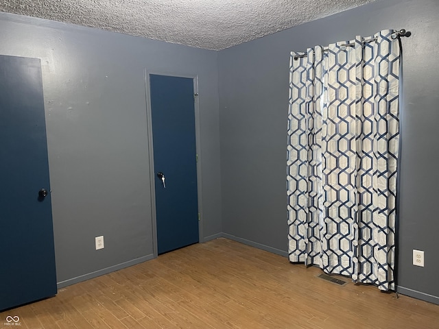 unfurnished room featuring visible vents, a textured ceiling, baseboards, and wood finished floors