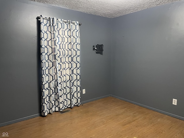 empty room featuring baseboards, wood finished floors, visible vents, and a textured ceiling